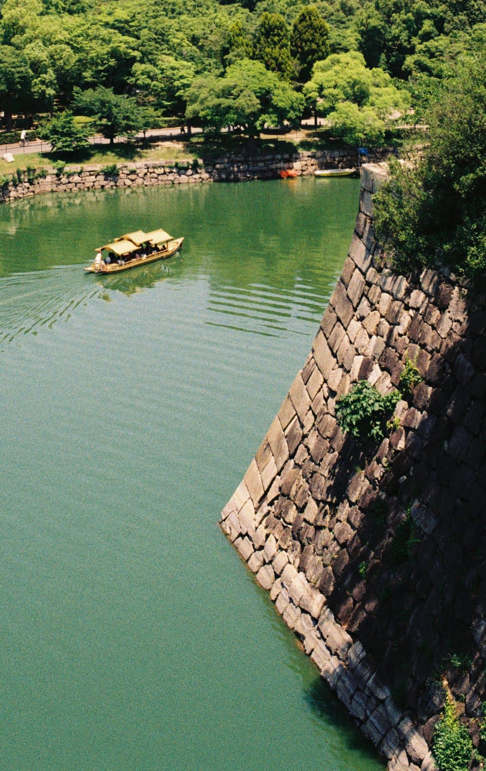 A small boat crossing the moat beneath the stone walls of Osaka Castle